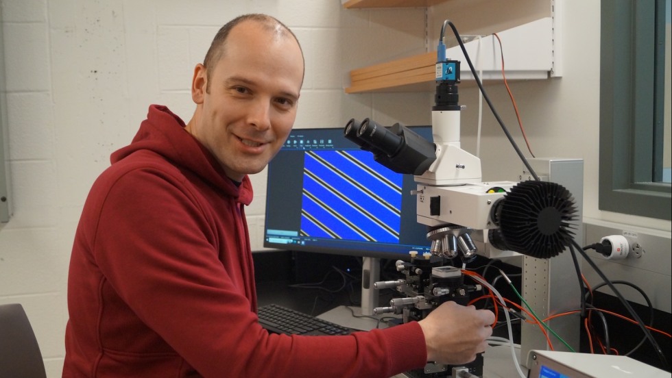 Matthias Kuehne sitting at table with a microscope in his lab.